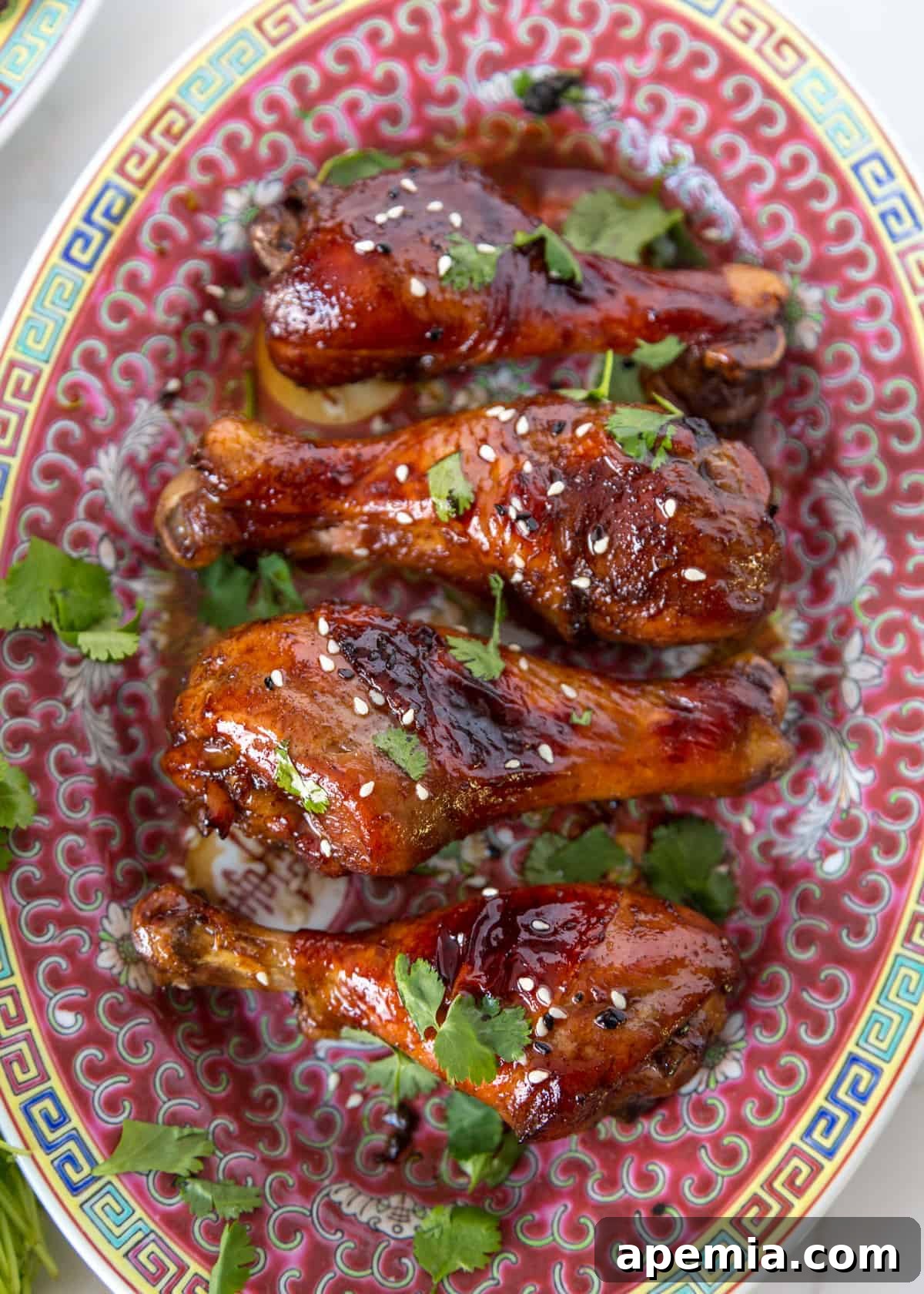 Overhead shot of sticky honey chicken drumsticks in a serving dish, garnished