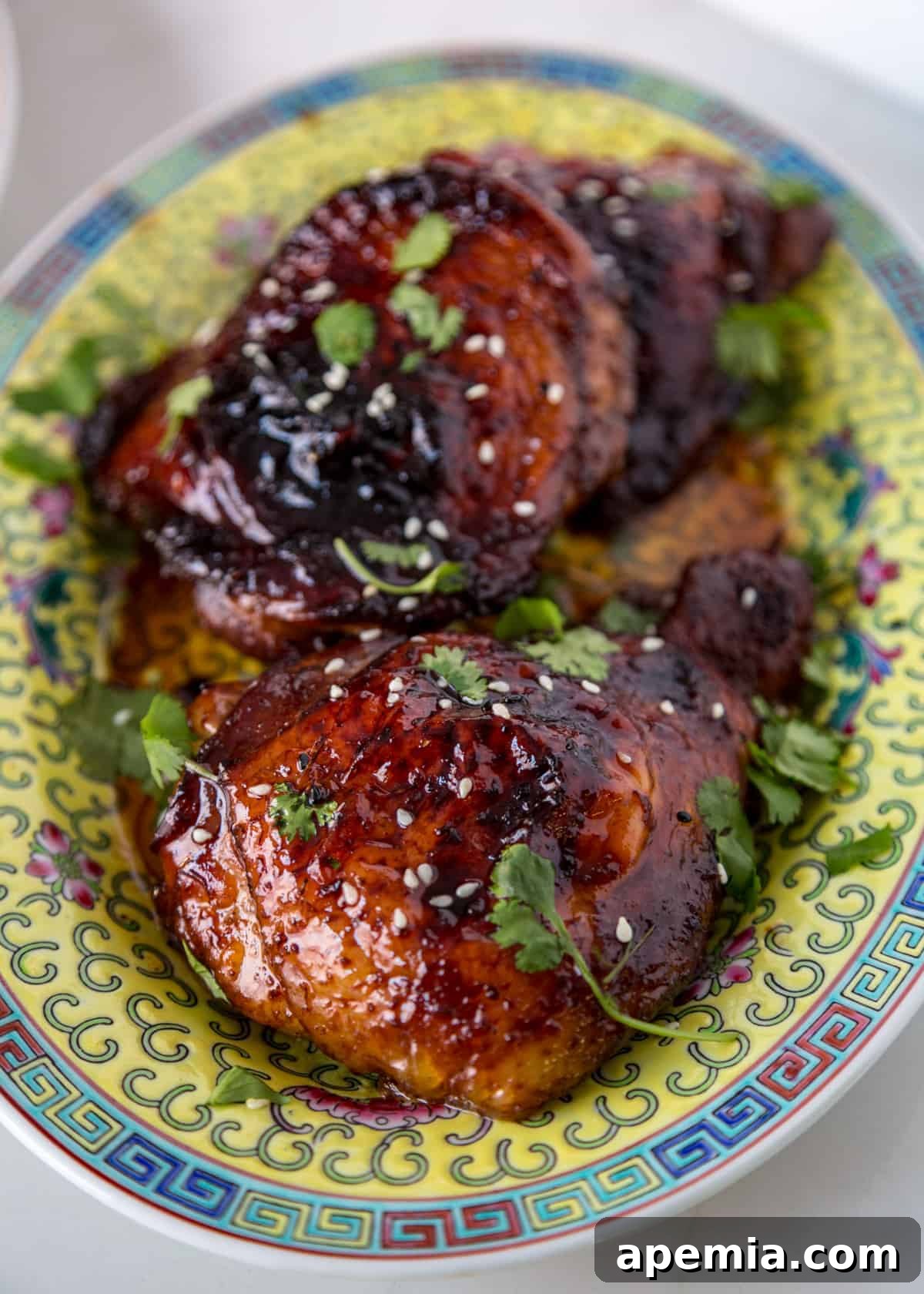 Plate with glistening honey glazed chicken thighs, garnished with sesame seeds