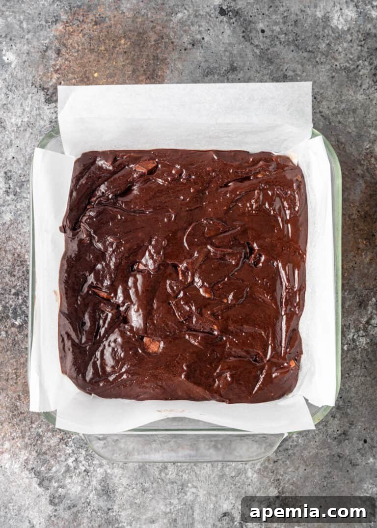 Process shot: Unbaked chocolate tahini brownie batter spread evenly in a parchment-lined baking pan.