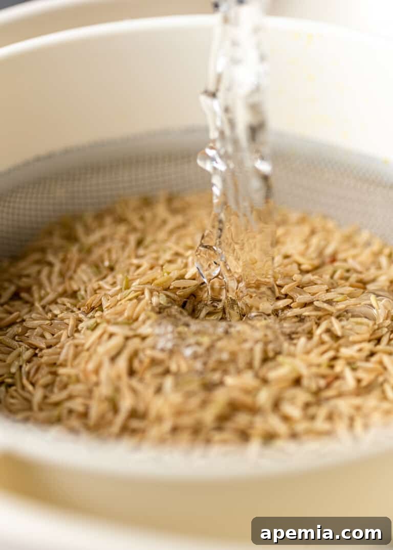 Brown basmati rice being rinsed in a mesh strainer under cold water.