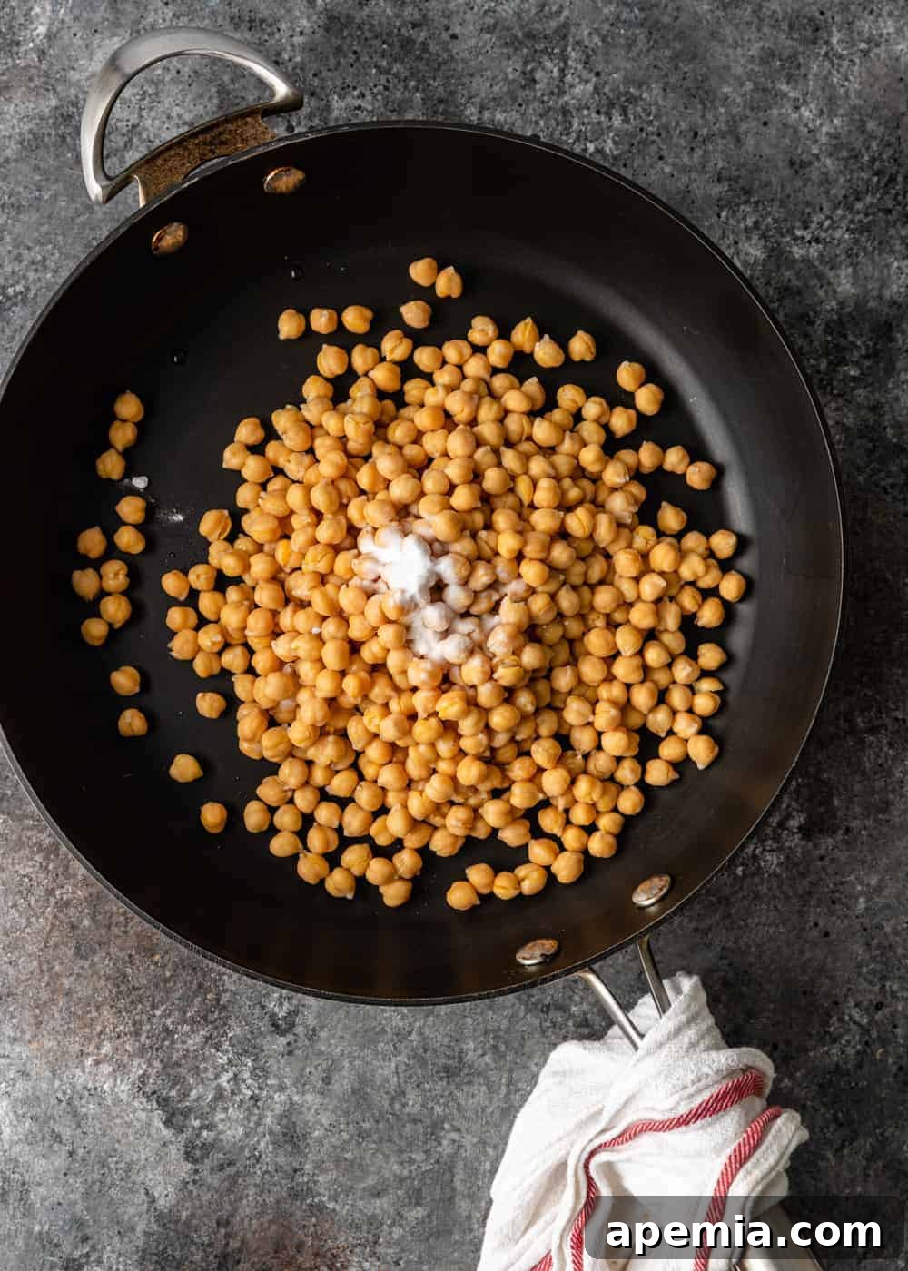 Close-up overhead shot of chickpeas being dry toasted in a skillet before boiling, showcasing the initial step for perfect hummus.