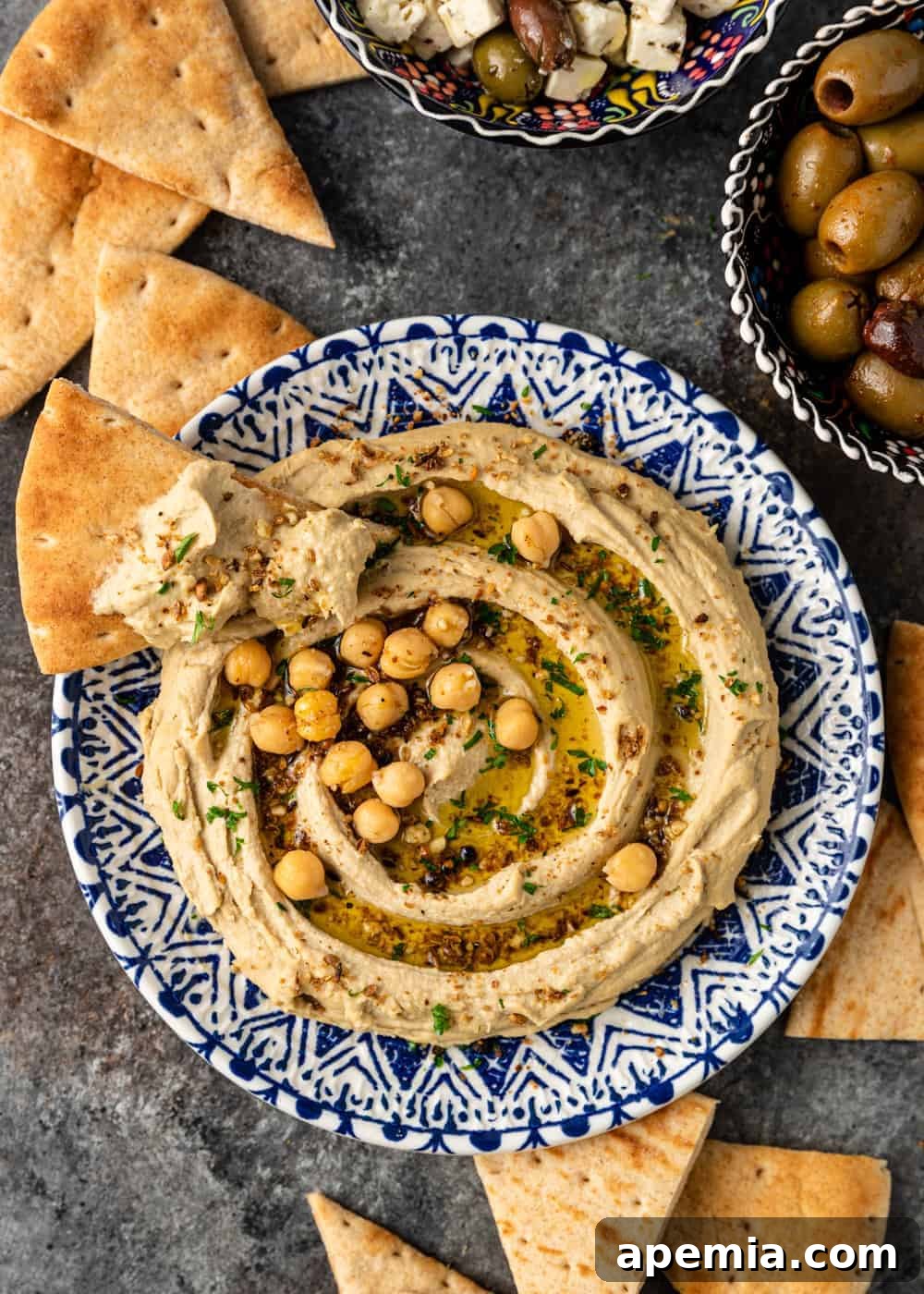 A close-up shot of creamy homemade hummus generously spread on a crispy pita chip, resting elegantly on the edge of a bowl filled with the fresh dip.