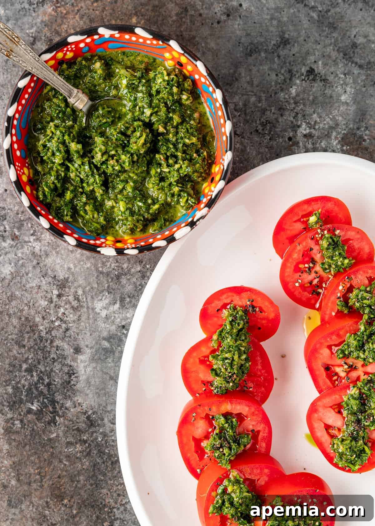 overhead: bowl of schug sauce spread over platter of cut tomatoes