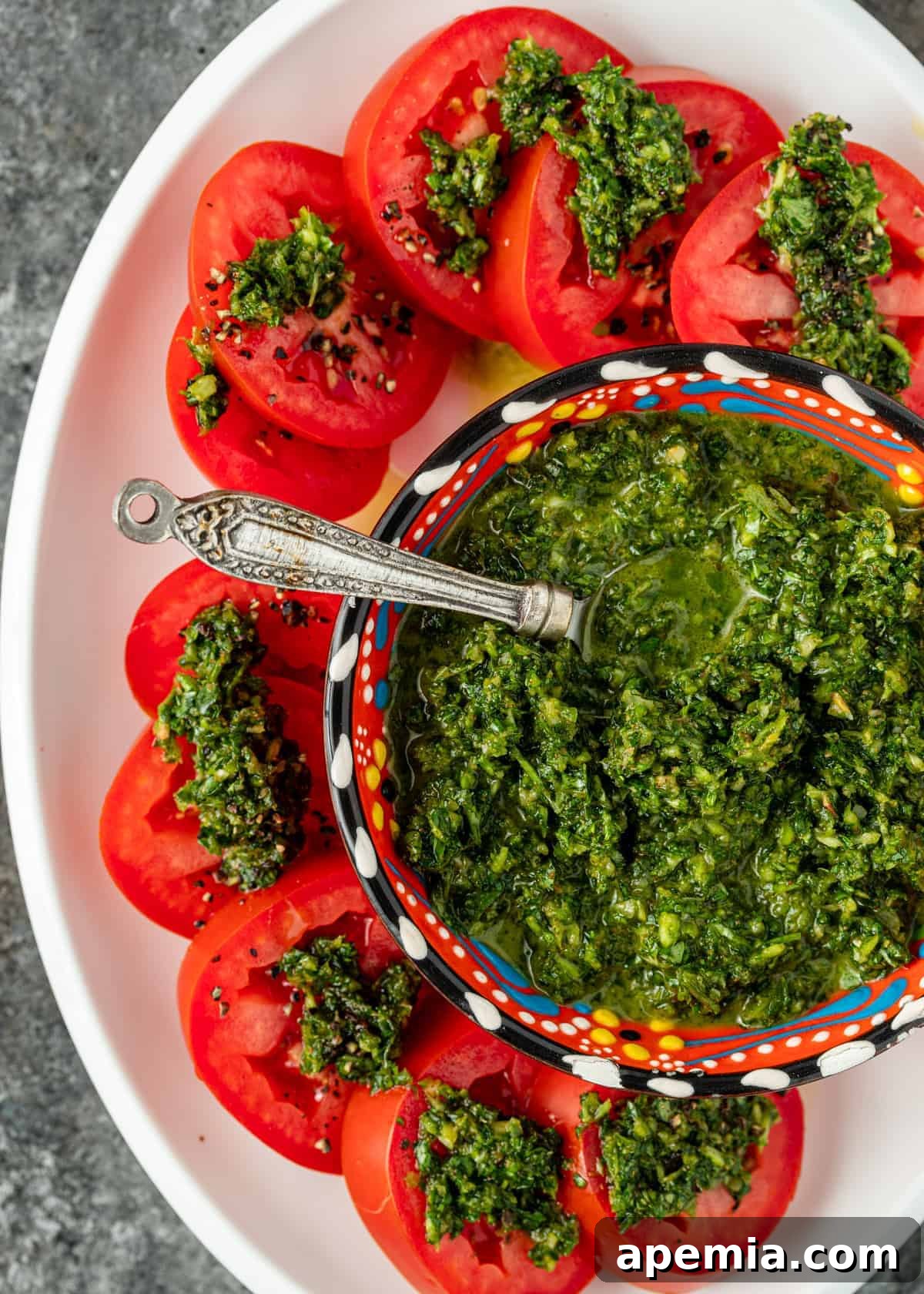 overhead: platter of cut roma tomatoes with bowl of zhoug
