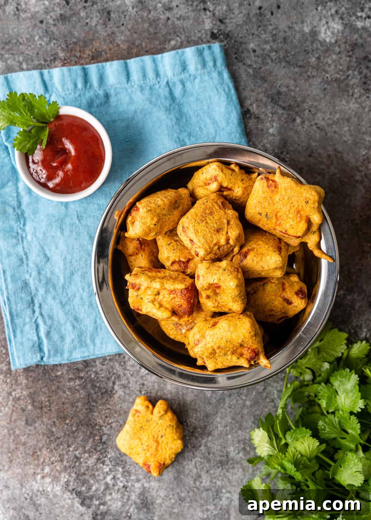 overhead: golden-brown fried paneer pakora neatly arranged in a metal bowl, ready to be served