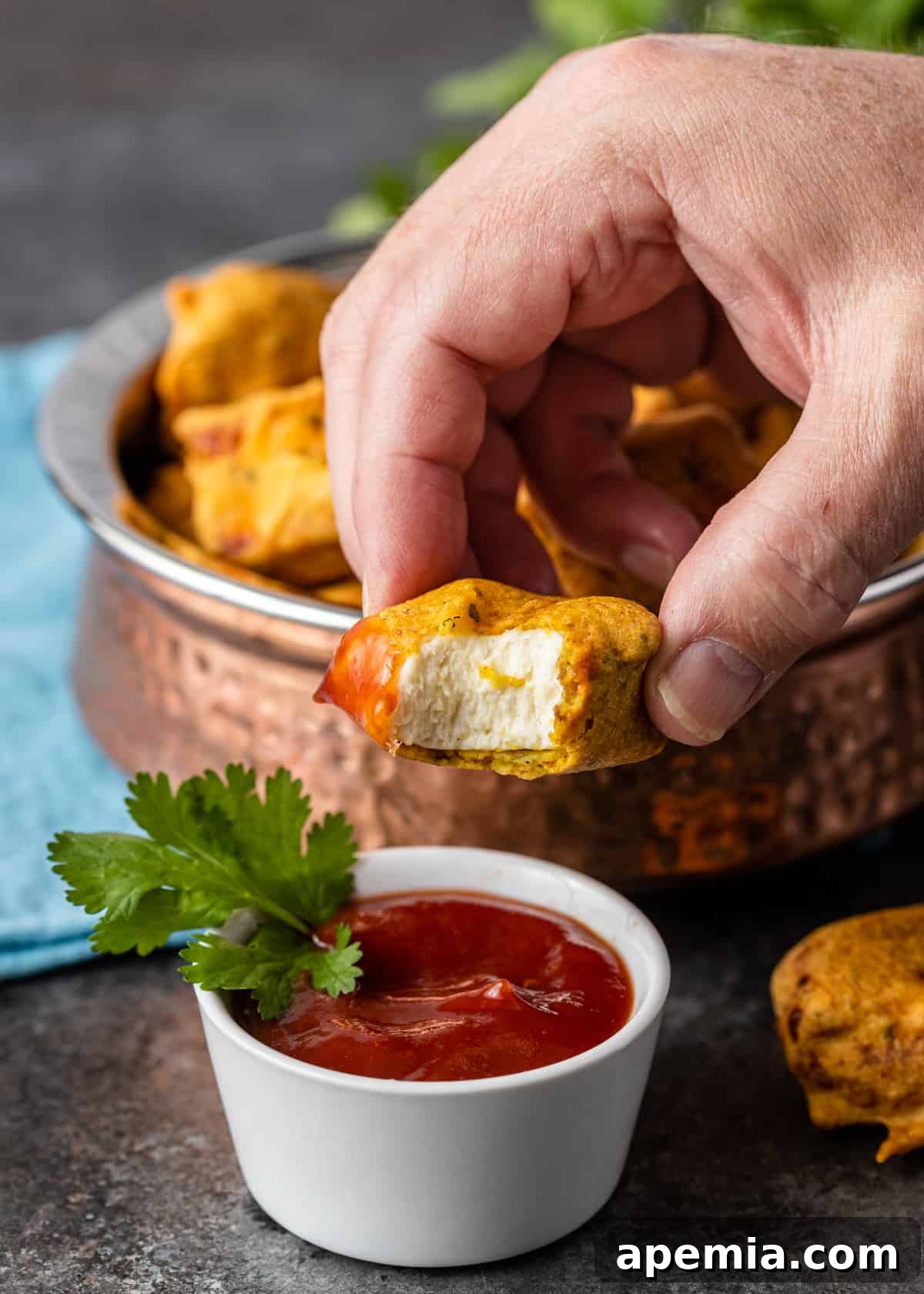 closeup: a delicious Indian cheese fritter with a bite taken out, revealing the soft paneer inside and the crispy batter