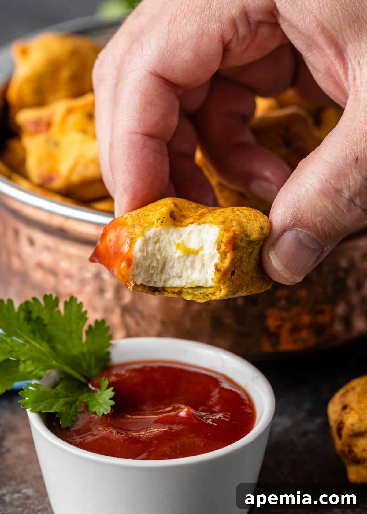 closeup: man's hand holding a golden-brown paneer fritter, emphasizing its inviting texture