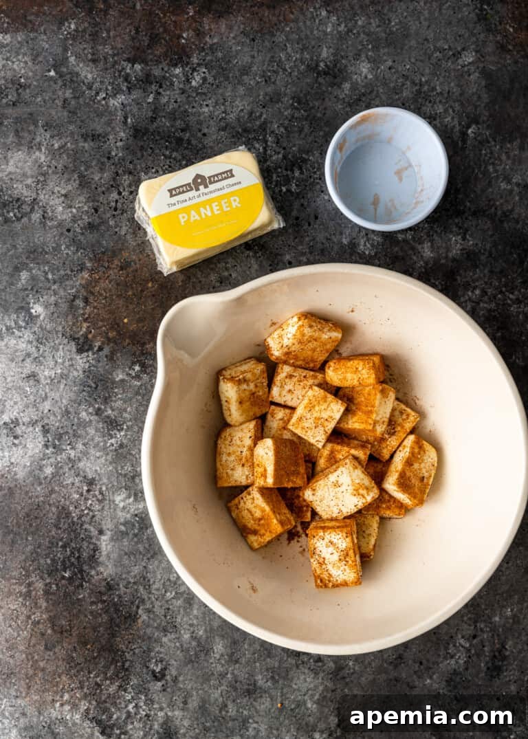 overhead process shot: cubed paneer being generously coated with a vibrant mix of Indian spices