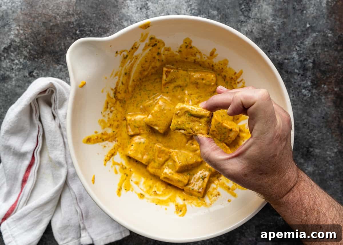 overhead process shot: a cube of paneer being carefully dipped into the prepared pakora batter