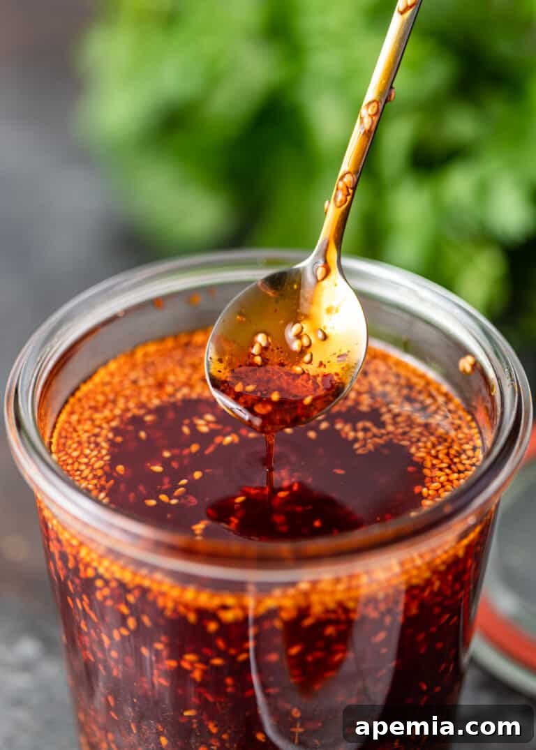 close up of chili crisp dripping from spoon into glass dish
