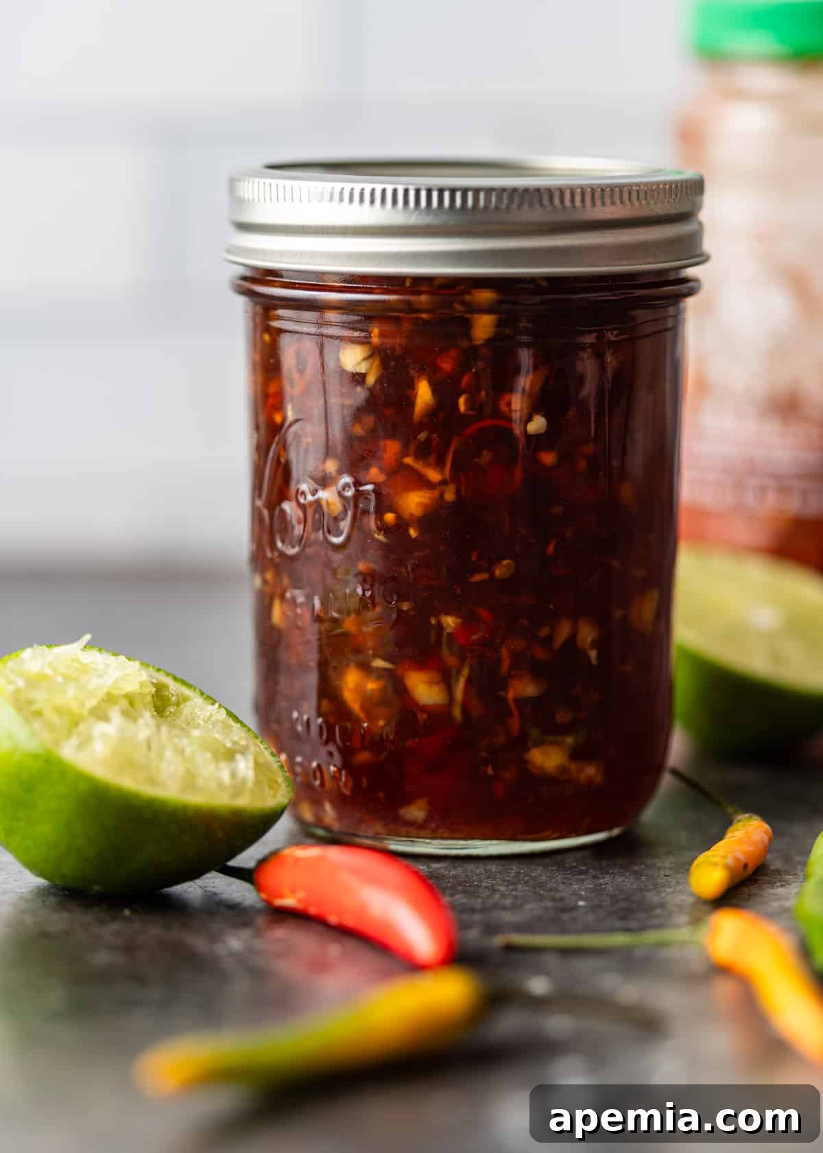 a mason jar full of vietnamese dipping sauce with lime and peppers to the side