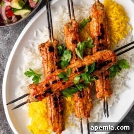 Overhead shot of Persian saffron chicken koobideh kabob on a platter with white and saffron rice, garnished with fresh herbs and lemon wedges.