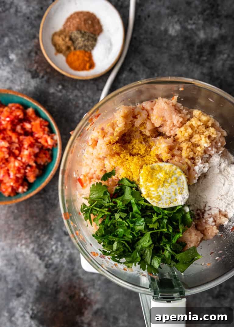 Overhead view of various chicken koobideh recipe ingredients being combined in a food processor.