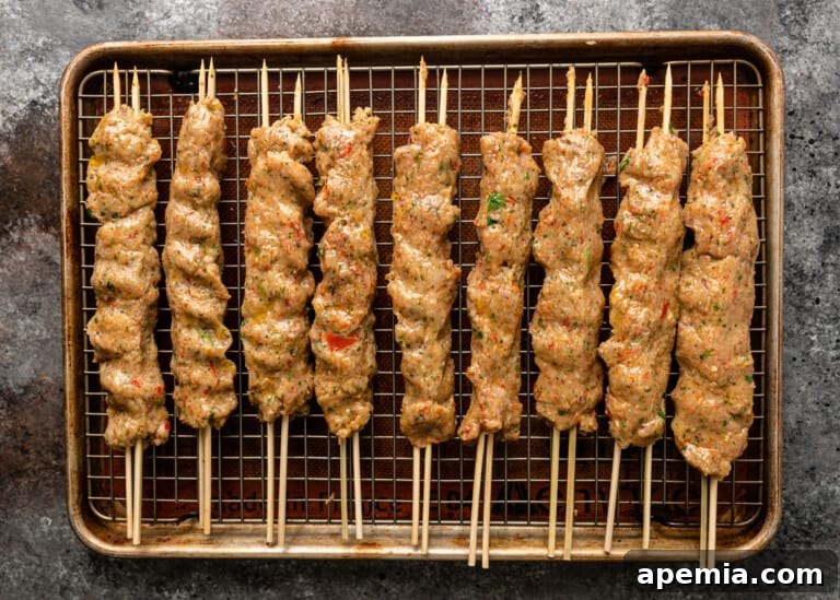 Overhead view of raw ground chicken kebabs meticulously shaped on flat skewers, resting on a baking sheet before cooking.