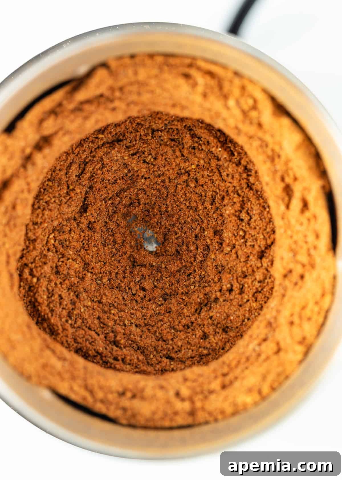 overhead: freshly ground homemade berbere spice blend in a spice grinder, showcasing its texture and vibrant color