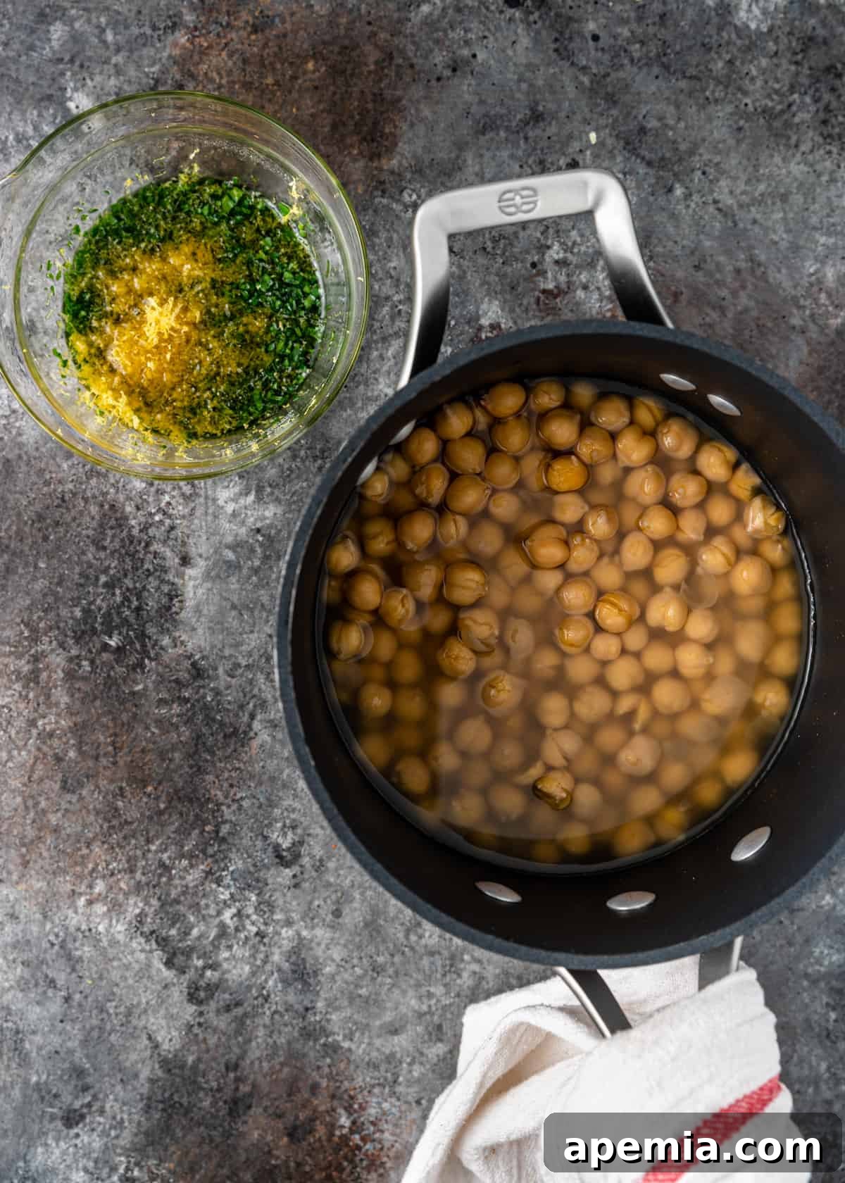 overhead process shot: bowl of fresh herbs and lemon peel next to pan of soaking chickpeas