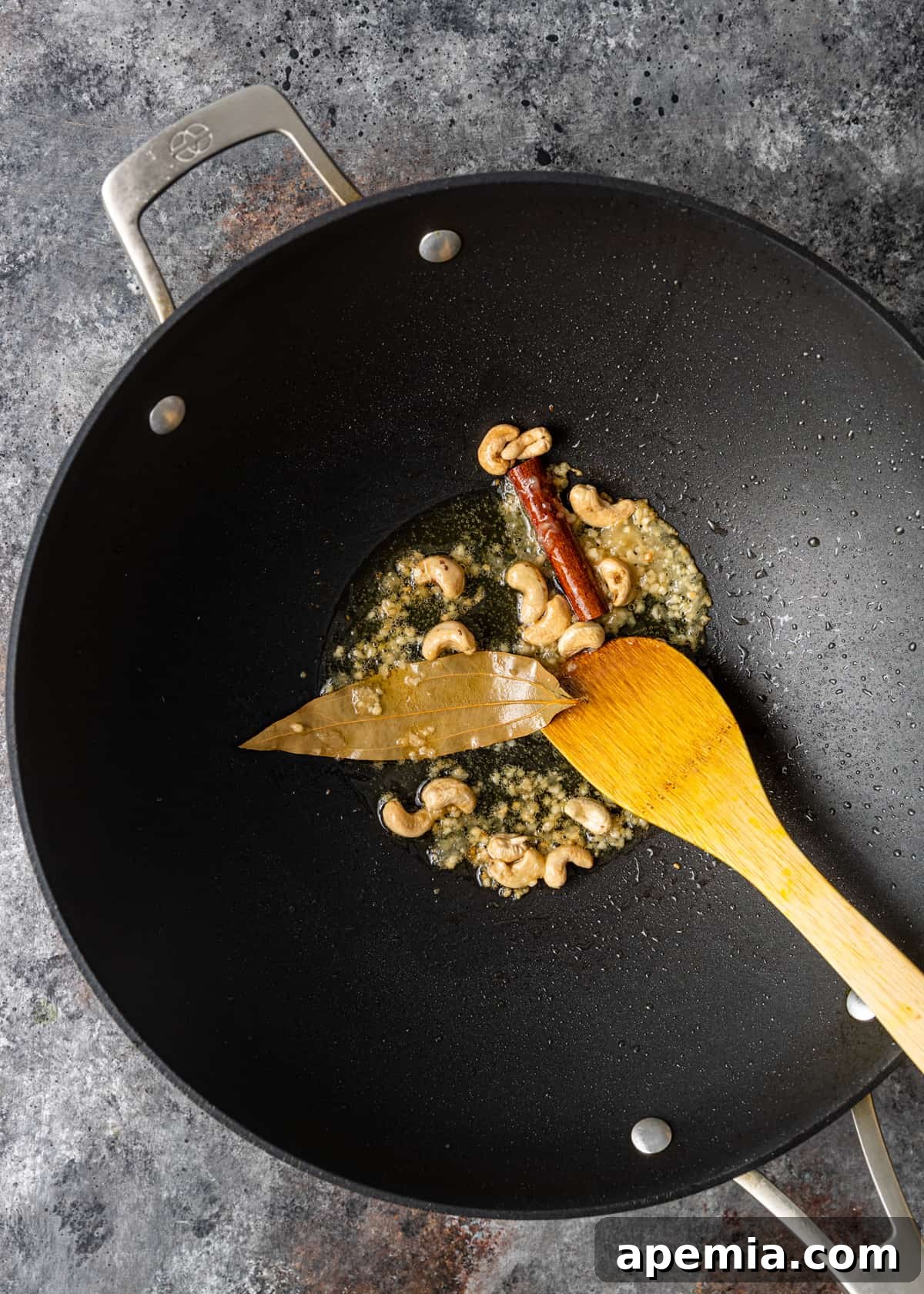 Overhead shot of whole spices and raw cashews frying in hot ghee or oil in a pan, releasing their aromas.