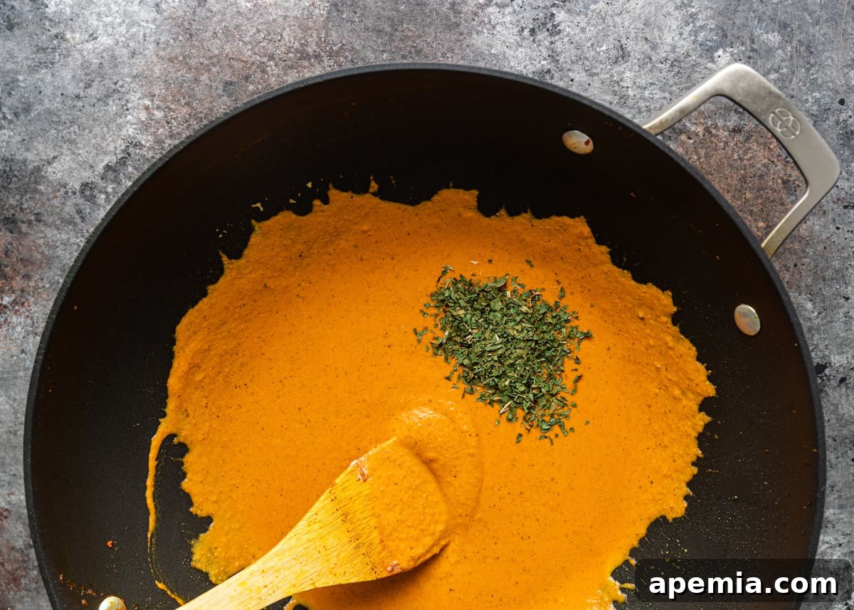 Overhead shot of an orange-colored sauce being stirred in a sauté pan, indicating the curry base is cooking down.