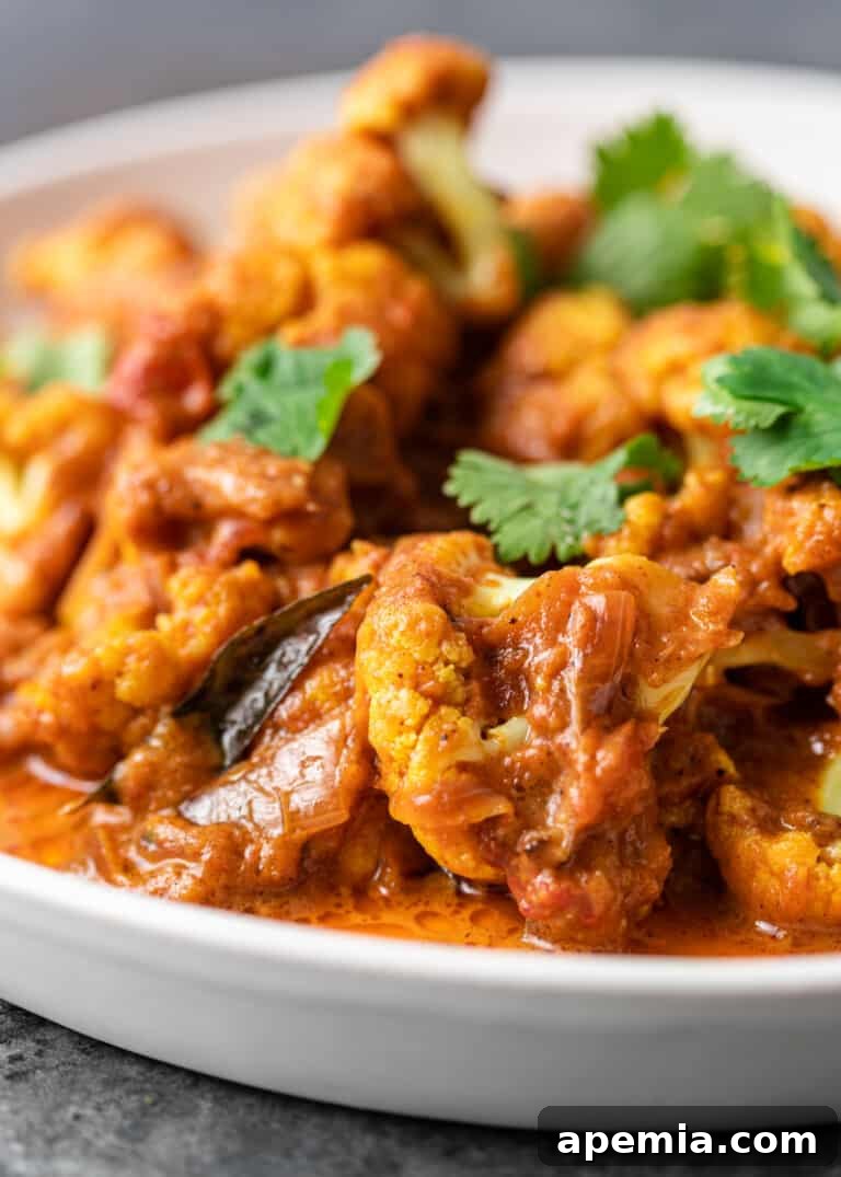 Close-up of a vibrant vegetarian Gobi Masala curry on a white plate, ready to be served, garnished with fresh cilantro.