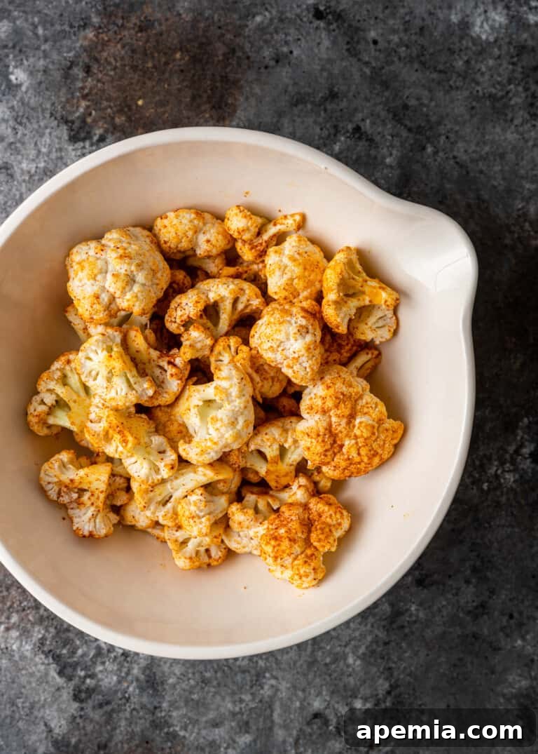 Cauliflower florets tossed in vibrant Indian spices, preparing for frying.