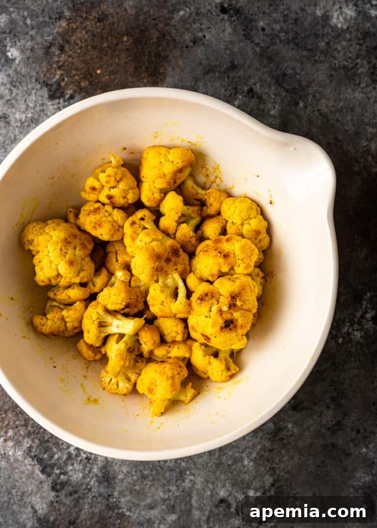Seasoned cauliflower florets in a pan, getting ready to be cooked for Gobi Masala.