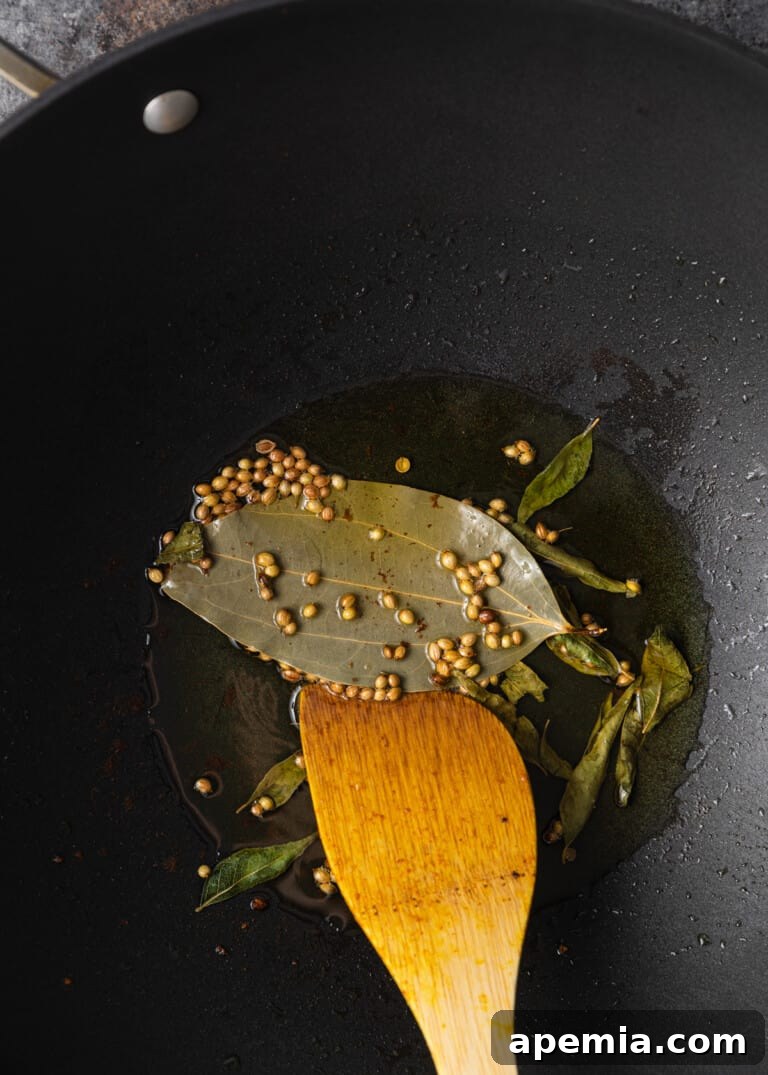 Sizzling whole spices frying in hot ghee, releasing their aromatic flavors.