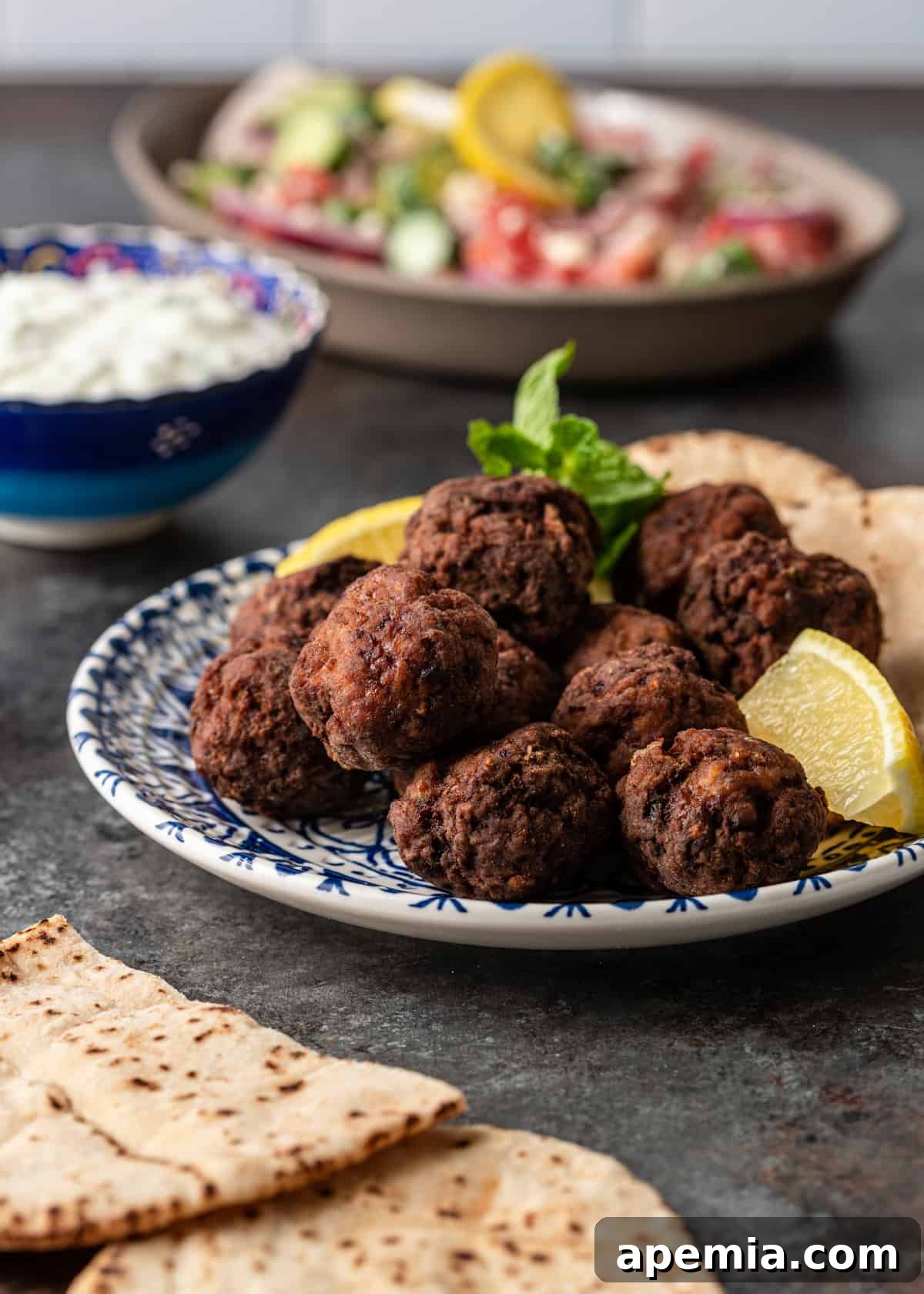 Authentic Pan-Fried Greek Lamb Keftedes 3 plate of freshly cooked pan fried Greek lamb meatballs with a lemon wedge and herbs, showcasing their vibrant presentation