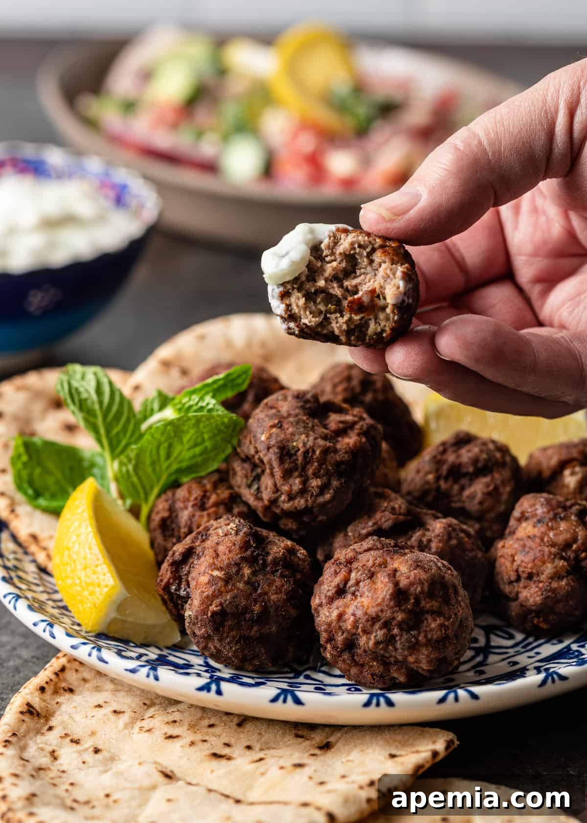 Authentic Pan-Fried Greek Lamb Keftedes 9 a hand lifting up keftedes dipped in sauce, showing the appealing texture and serving suggestion