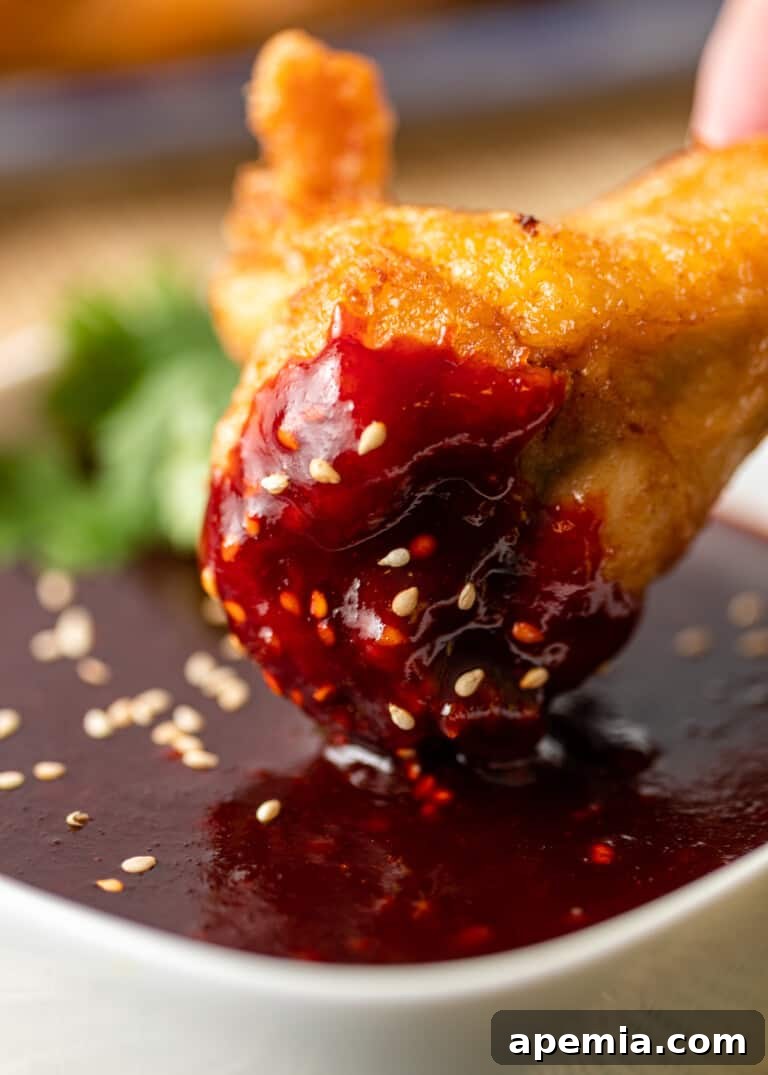 Close-up view of a golden-brown crispy chicken wing being dipped into a small bowl of vibrant, homemade Korean Gochujang Sauce, highlighting the sauce's thick and smooth texture.