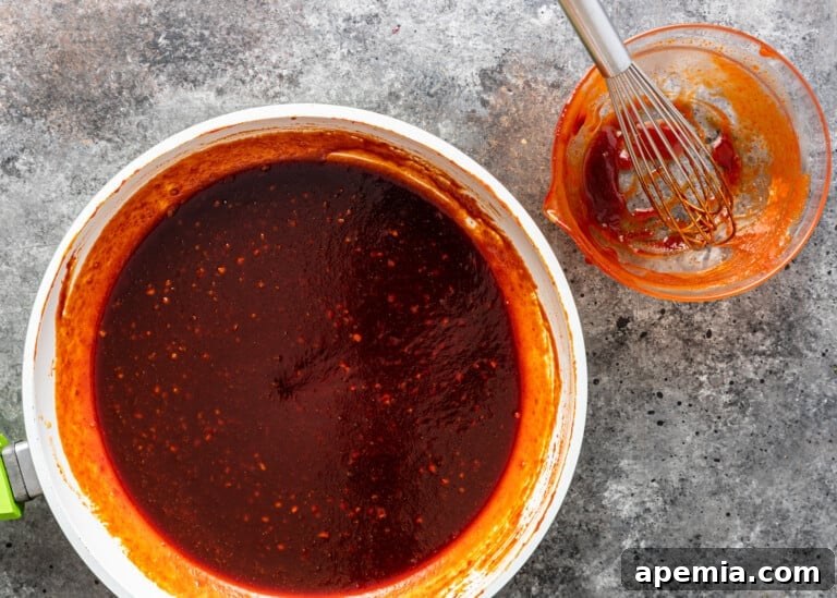 Overhead shot of a clear plastic container filled with freshly prepared, vibrant red Korean Gochujang Sauce, showcasing its smooth and appealing texture, ready for use.