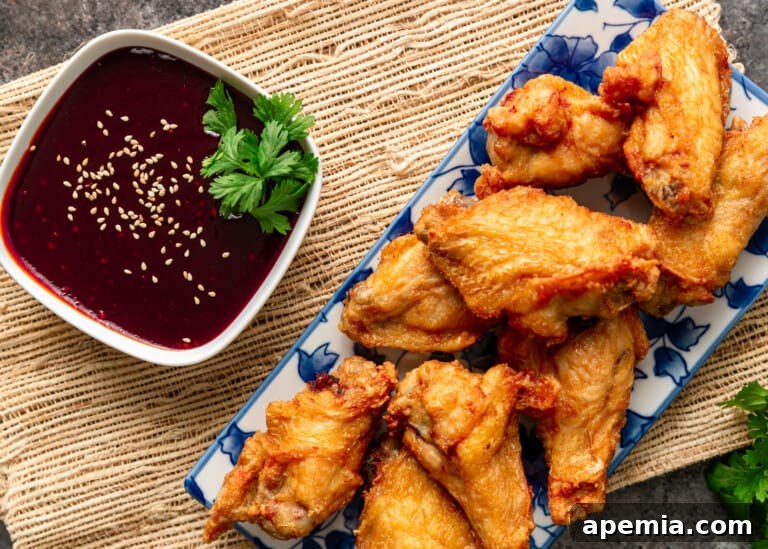 A beautifully arranged serving of crispy, golden-brown chicken wings perfectly complemented by a small, elegant bowl of rich, red Korean Gochujang Sauce, inviting immediate indulgence.