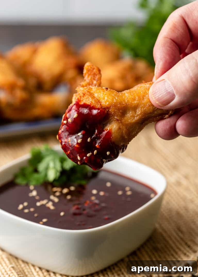A tantalizing image of a crispy fried chicken drumstick being dipped into a small, inviting bowl of vibrant Korean Gochujang Sauce, showcasing its perfect consistency for dipping.