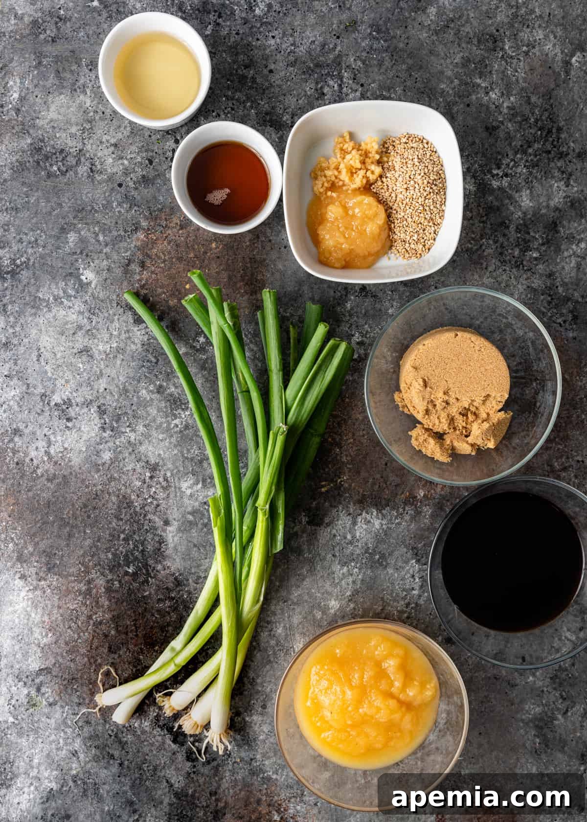 Overhead shot showcasing all the fresh ingredients laid out for making bulgogi sauce: soy sauce, brown sugar, applesauce, rice wine vinegar, ginger, garlic, sesame seeds, sesame oil, and scallions.