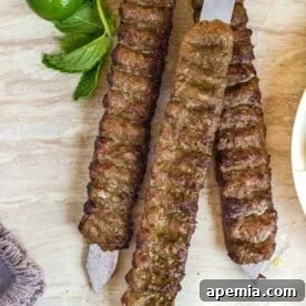 Overhead view of flat metal skewers holding perfectly cooked Koobideh kabobs on a rustic wooden table, garnished with fresh herbs and citrus.