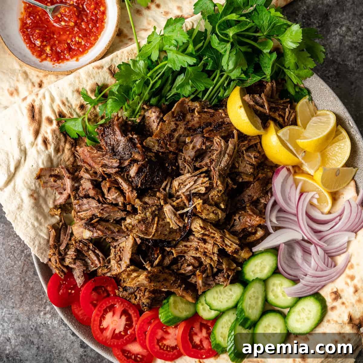 Overhead shot of a platter with shredded lamb shawarma, fresh vegetables, and sauces, ready to be served in pita bread.