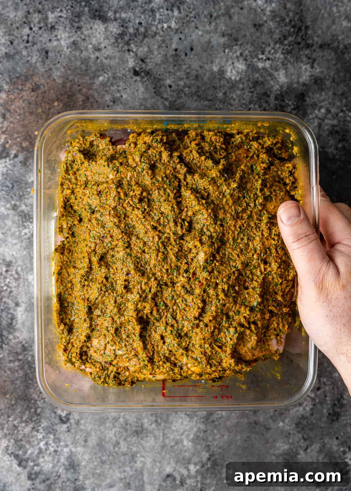 Overhead process shot showing a vibrant green herb and spice paste in a white dish, ready for marinating the lamb.