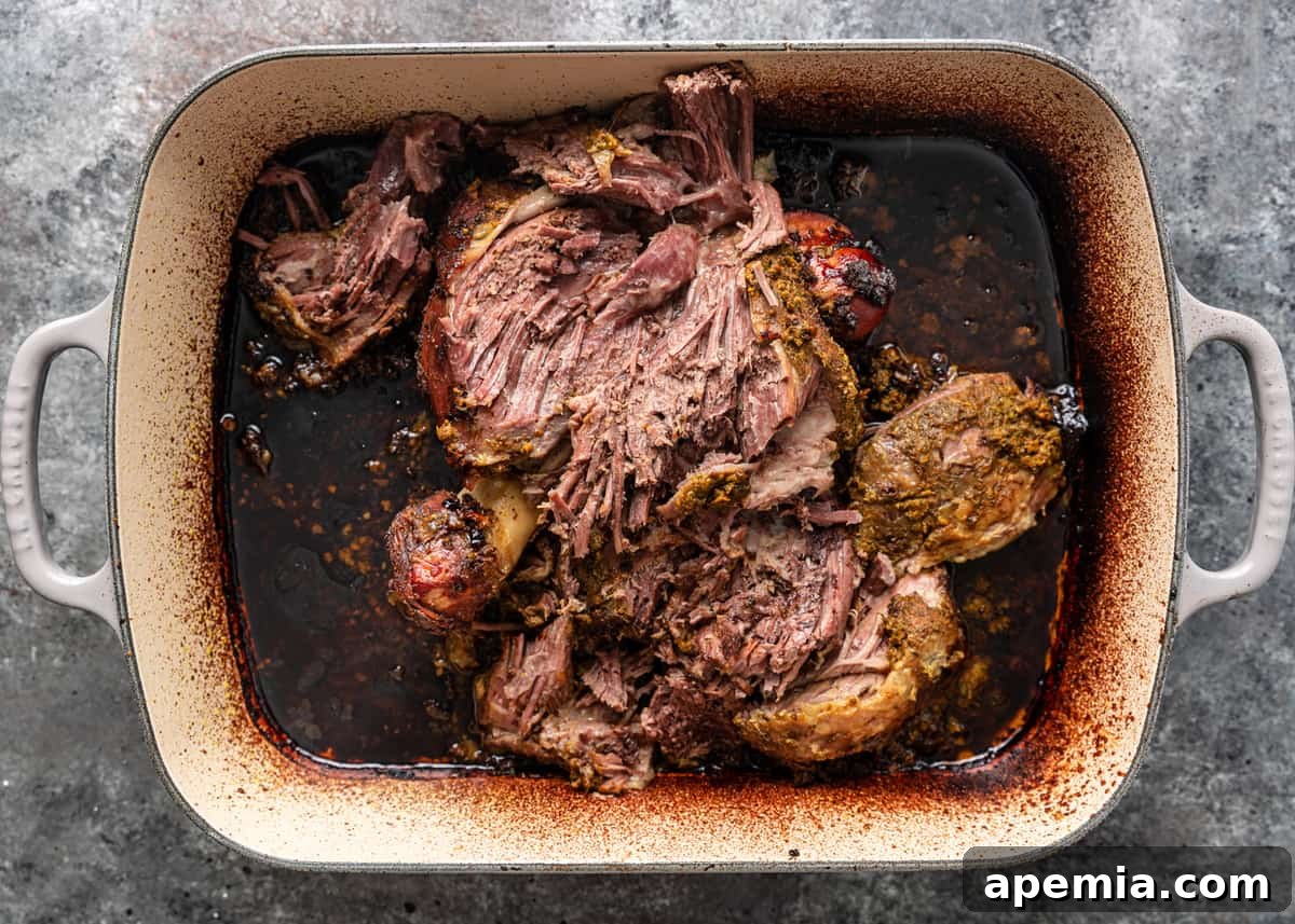 Overhead process shot of roasted, fall-apart tender lamb shawarma meat in a pan, still with its cooking juices, ready to be shredded.