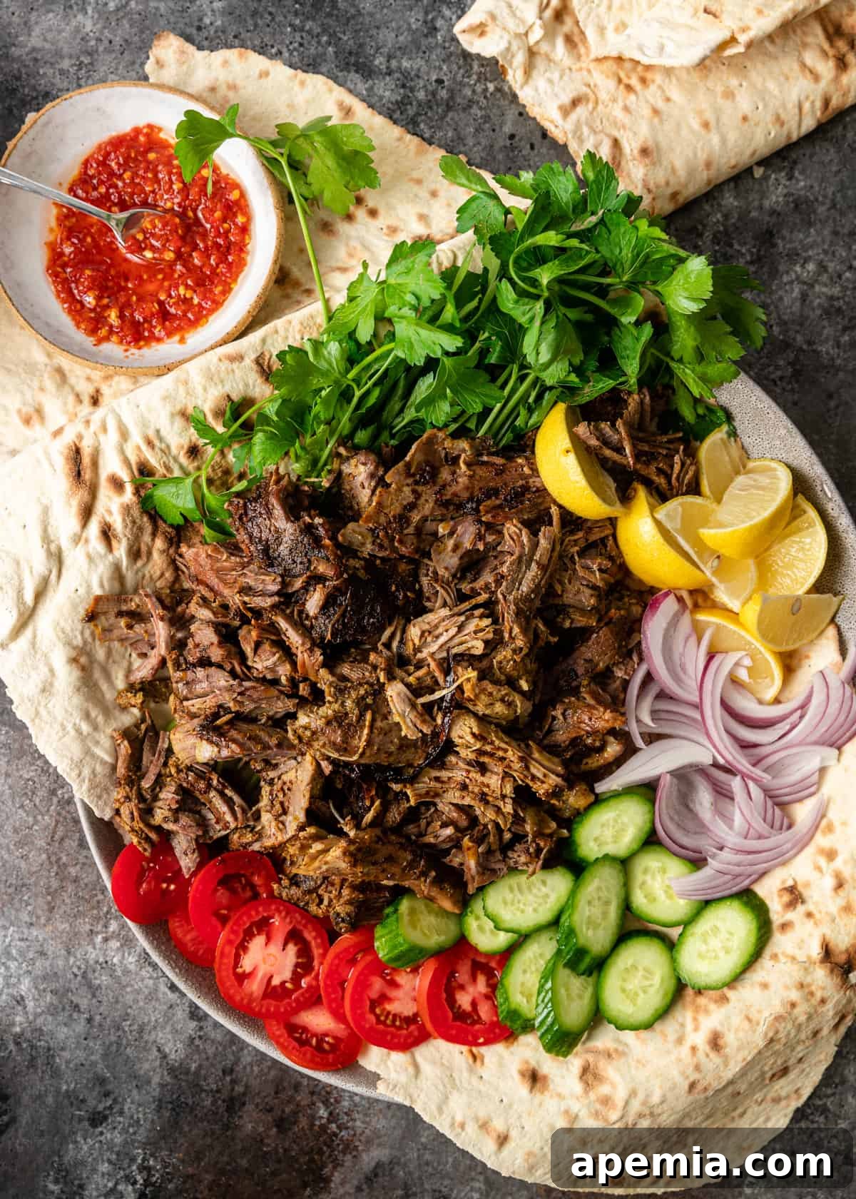 Overhead shot of a meticulously arranged platter featuring shredded lamb shawarma with an array of fresh toppings like tomatoes, cucumbers, and sauces, ready to be assembled into wraps.