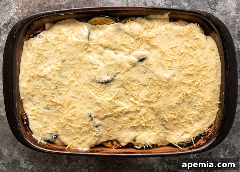 A thick, creamy béchamel sauce generously topping the moussaka layers before baking.