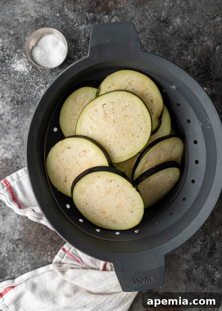 Sliced eggplant resting in a colander, draining excess liquid after salting.