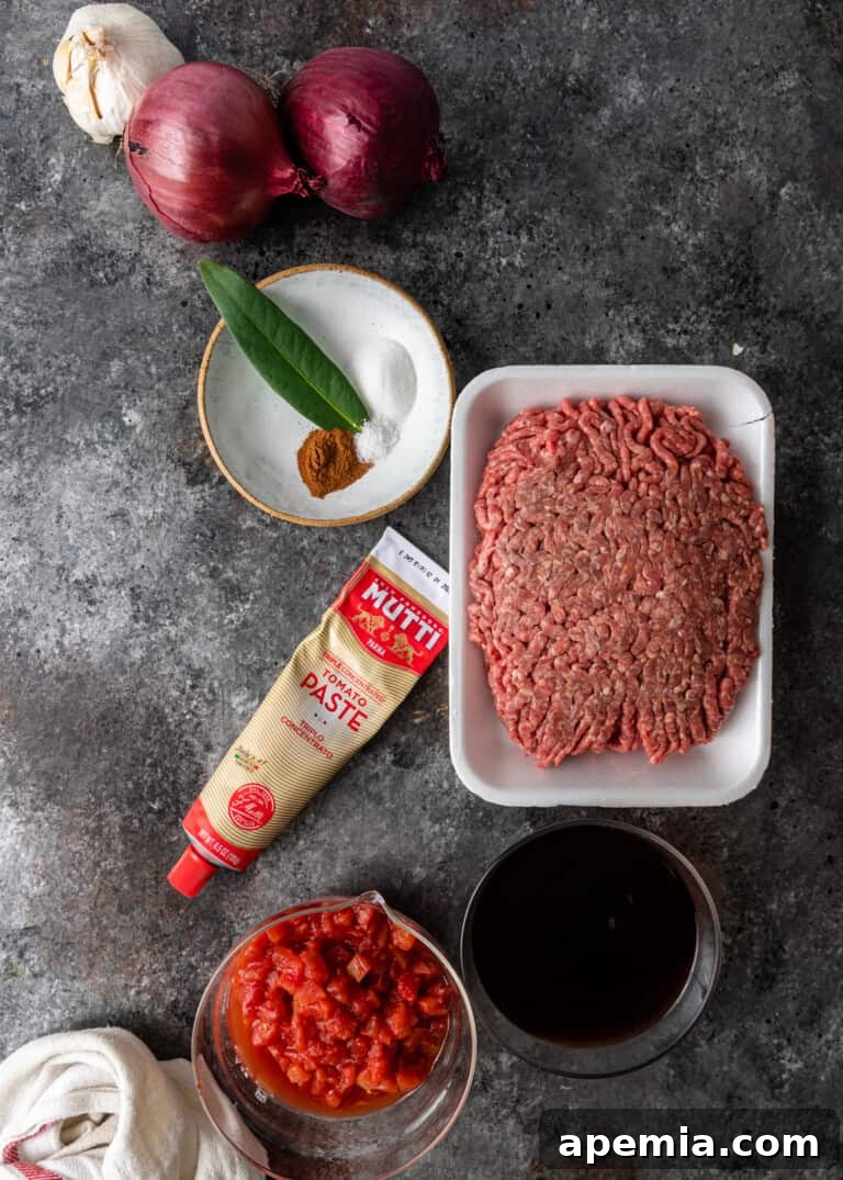 A collection of fresh ingredients laid out for preparing Greek moussaka, including eggplants, potatoes, and spices.