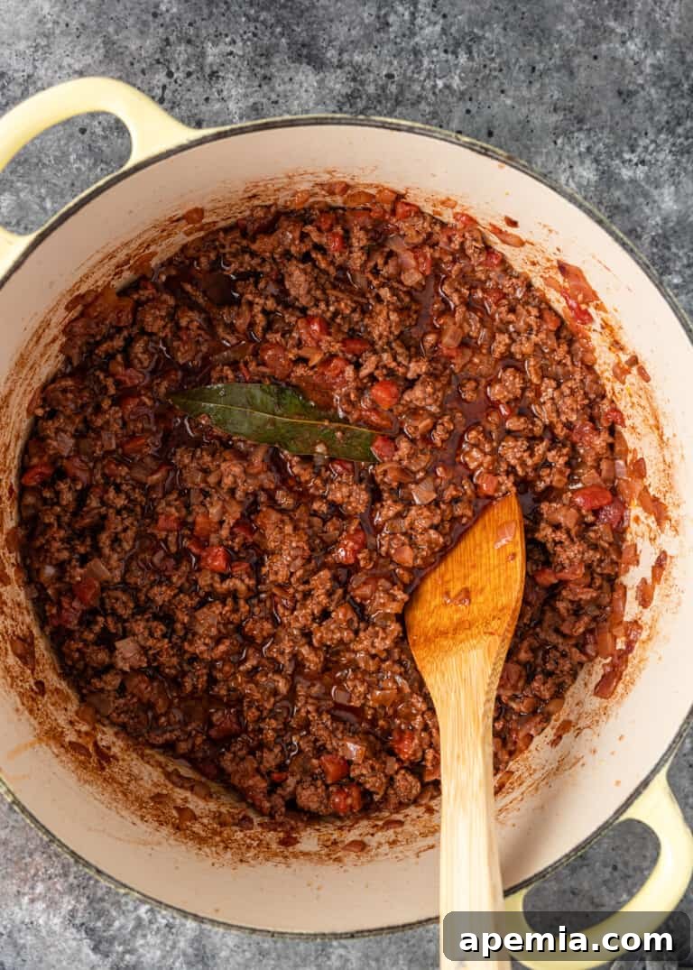 Rich meat sauce simmering in a pan, infused with Greek spices for moussaka.
