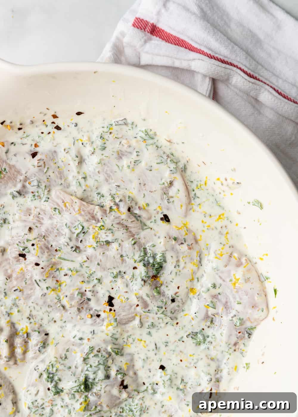 Overhead shot of chicken pieces being generously coated in a creamy Greek yogurt marinade in a bowl.