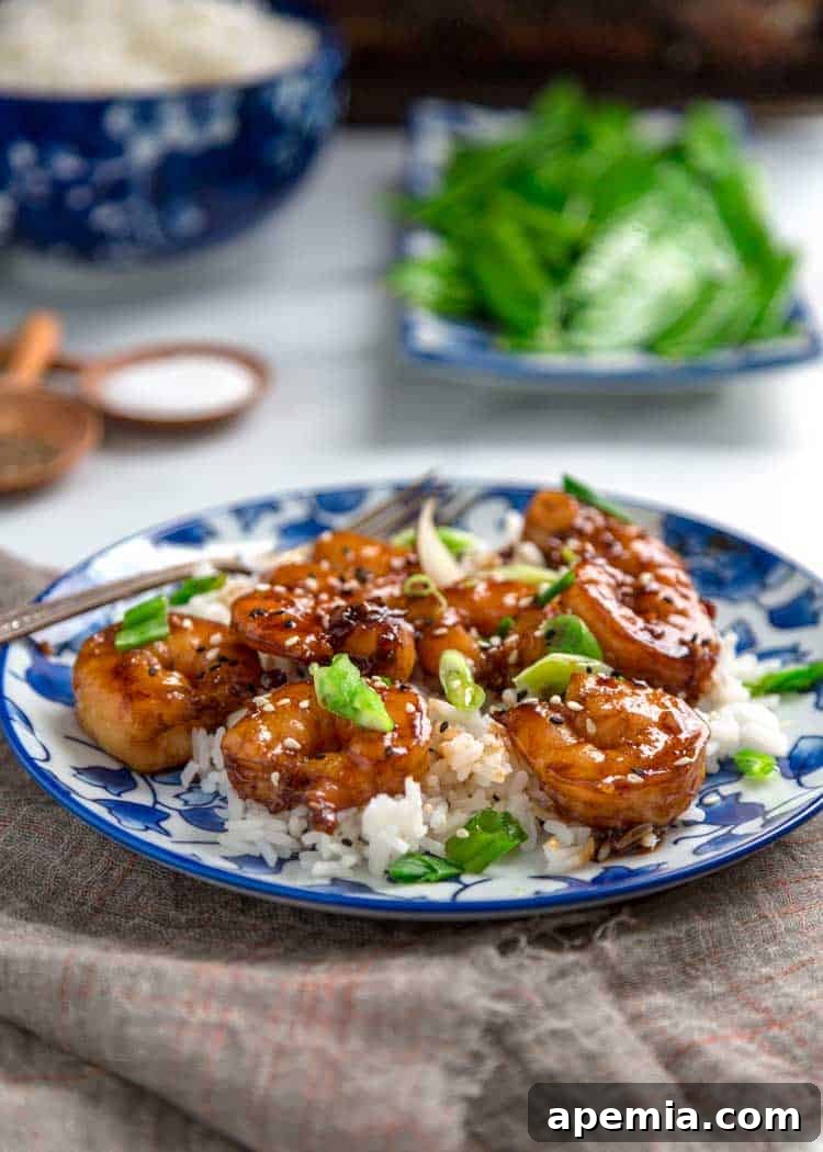 A serving of honey garlic shrimp artfully arranged on a bed of fluffy white rice, garnished with green onions and sesame seeds.