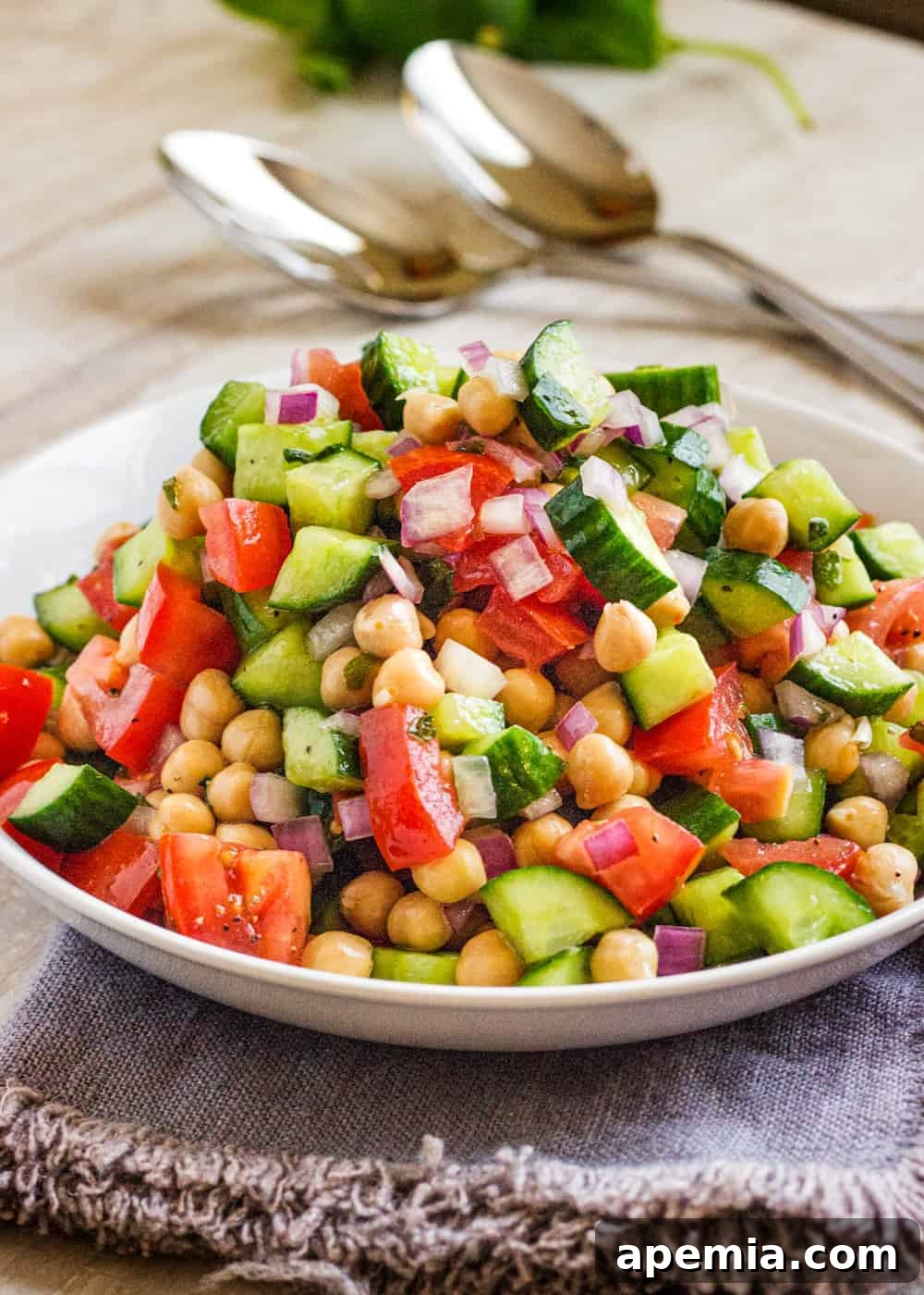 chopped vegetable and chickpea salad in a white bowl with metal spoons in the background