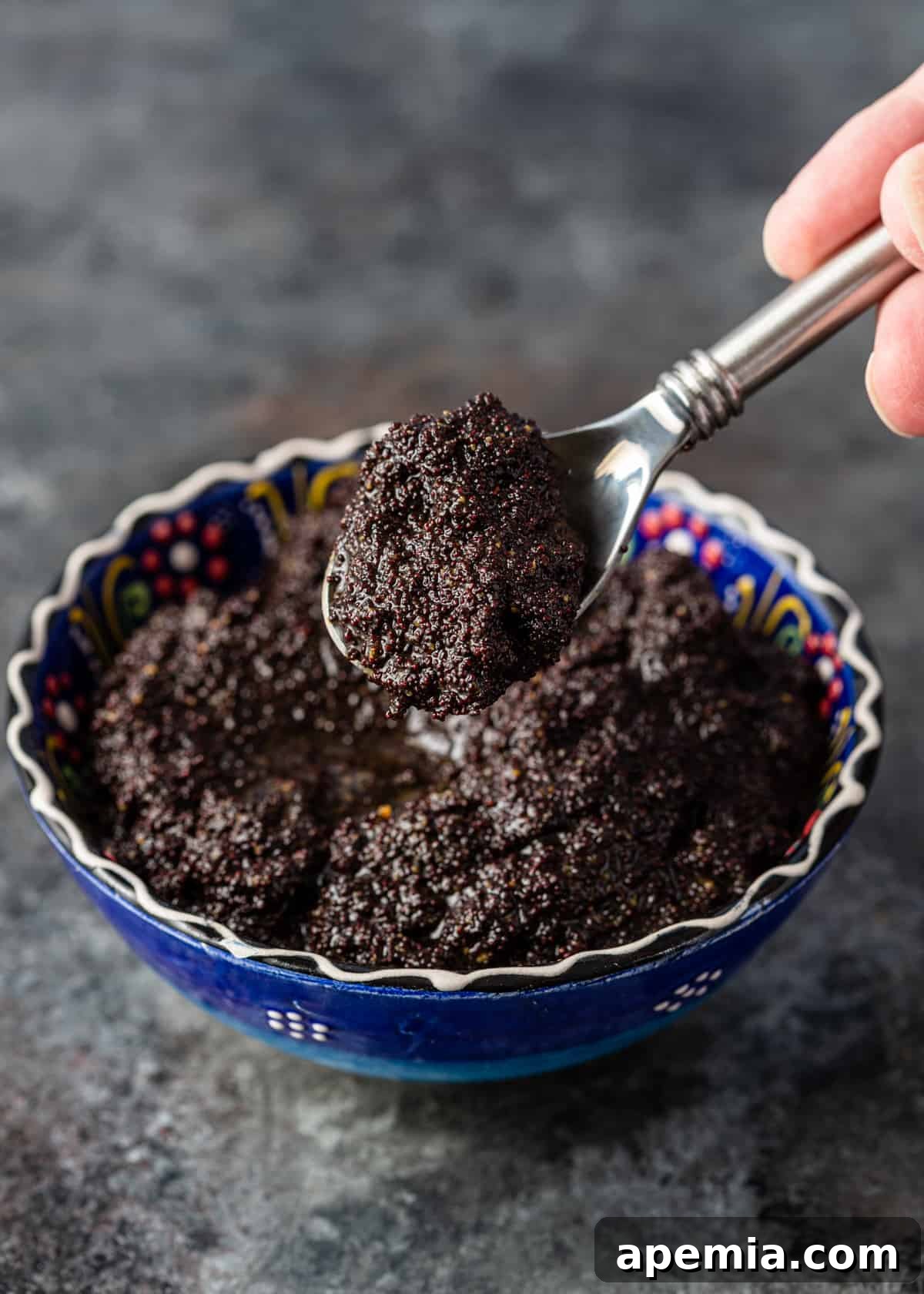 A spoon laden with rich, dark poppy seed paste, highlighting its smooth, spreadable consistency.