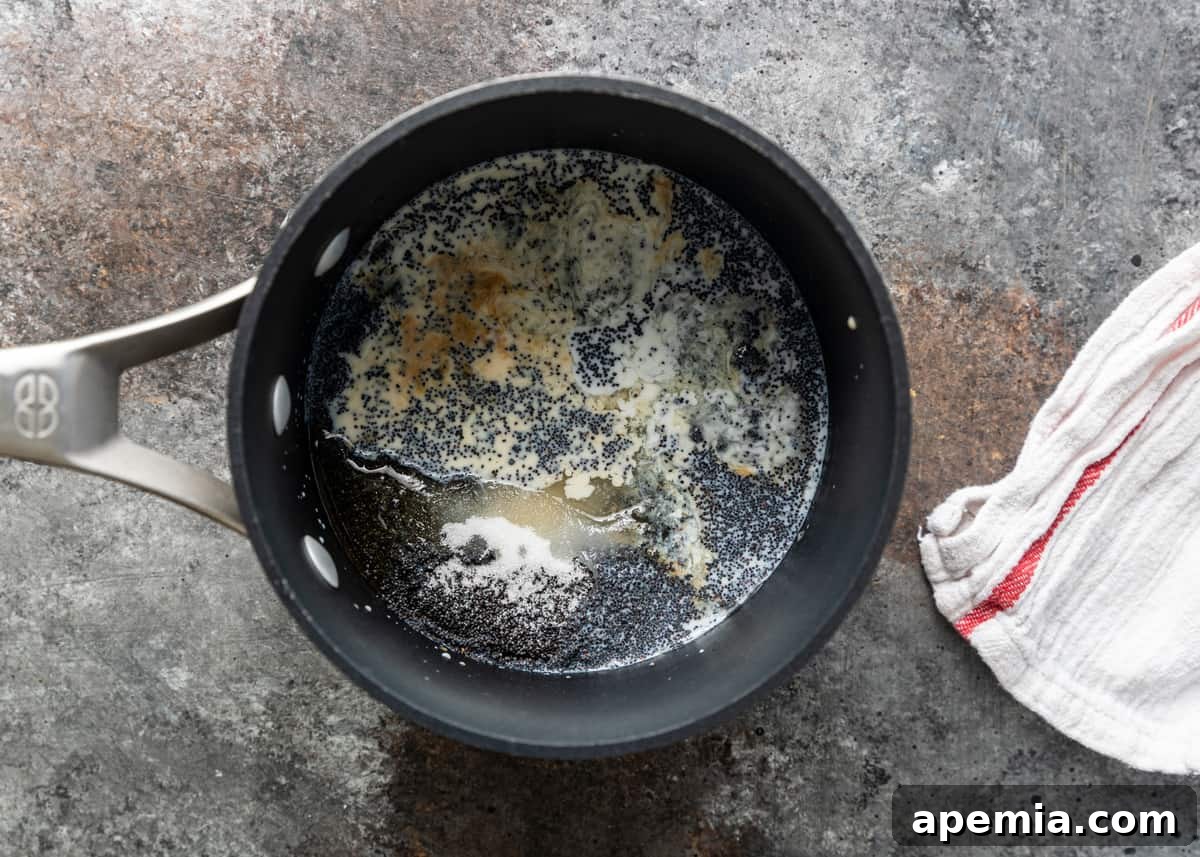 Overhead shot of all ingredients for mohn paste, including ground poppy seeds, milk, honey, and lemon juice, in a saucepan ready for cooking.