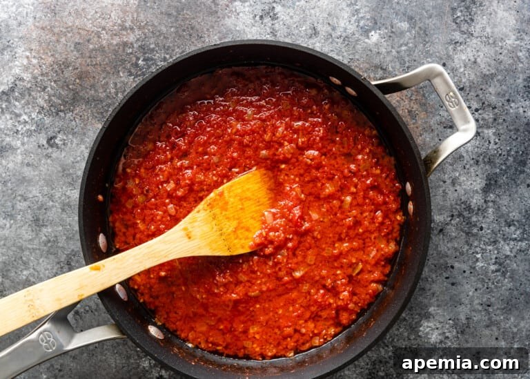 overhead: sautéed onion, garlic, and tomatoes in a pot with a wooden spoon