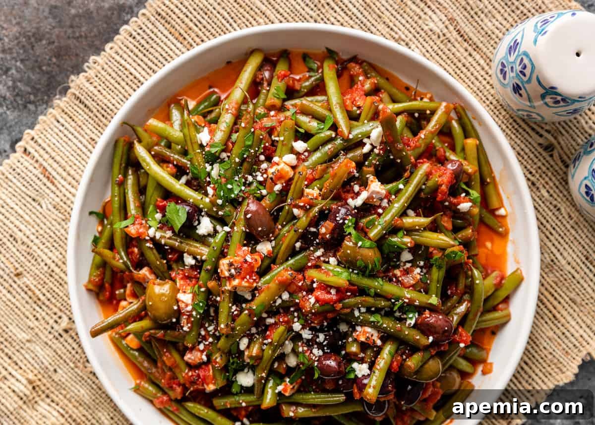 overhead: tossed fasolakia in a large white serving dish with olives and feta on top