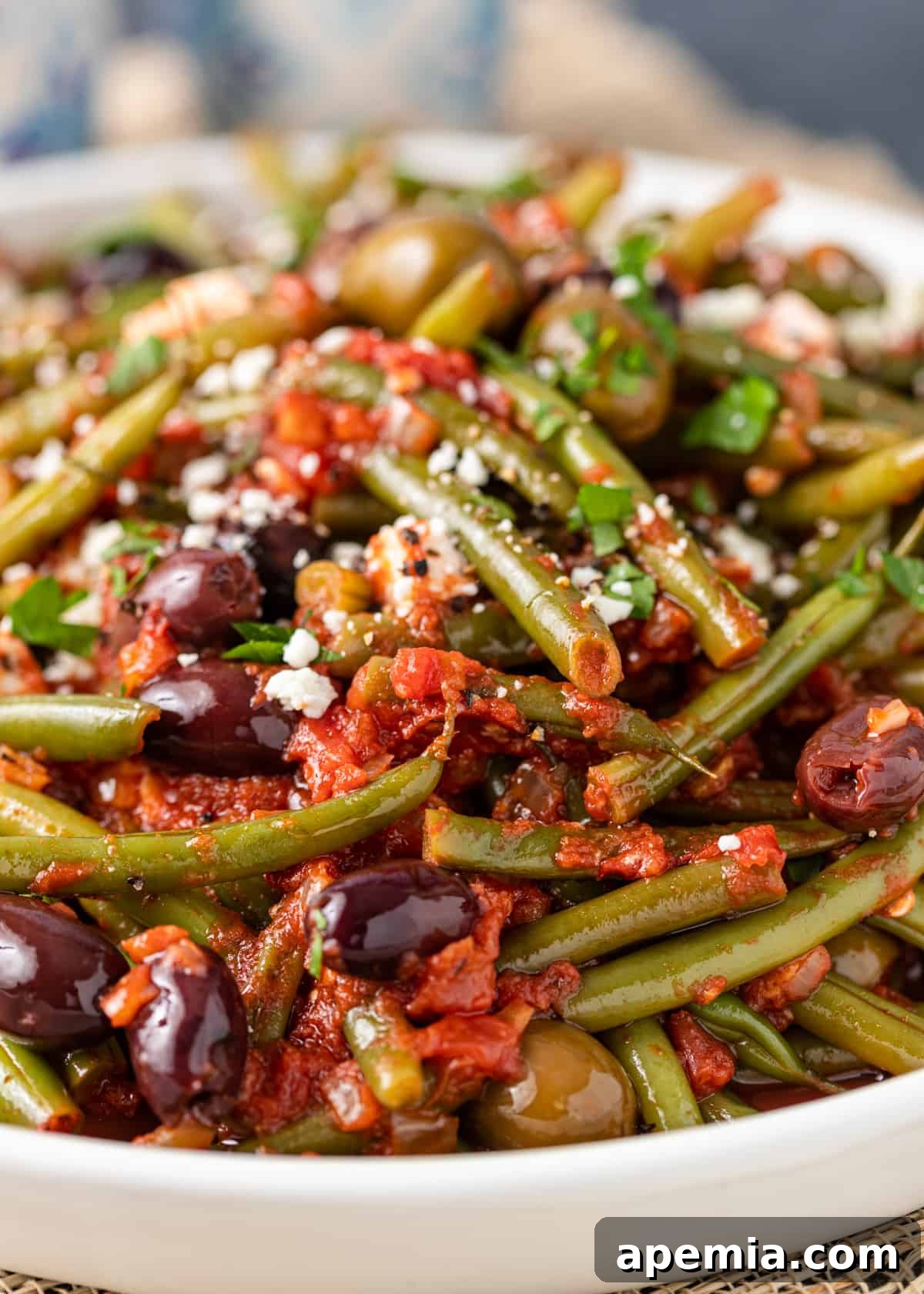 closeup: greek green beans in a large white serving dish with olives and feta on top